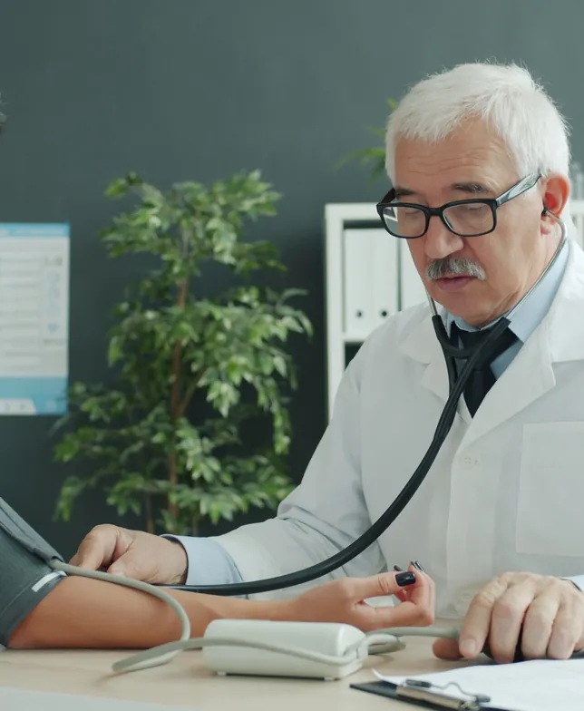 A doctor in a white coat taking a woman's blood pressure at his desk