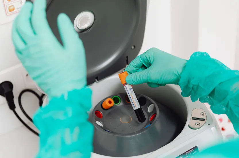 A gloved hand placing a blood sample tube into a laboratory centrifuge