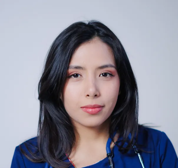 A doctor with long dark hair in navy scrubs, looking straight at the camera