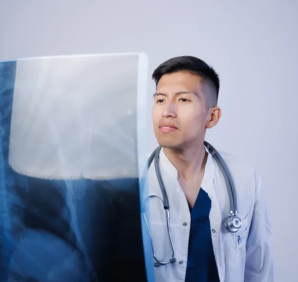 A young doctor in a white coat holding up a chest X-ray to the light